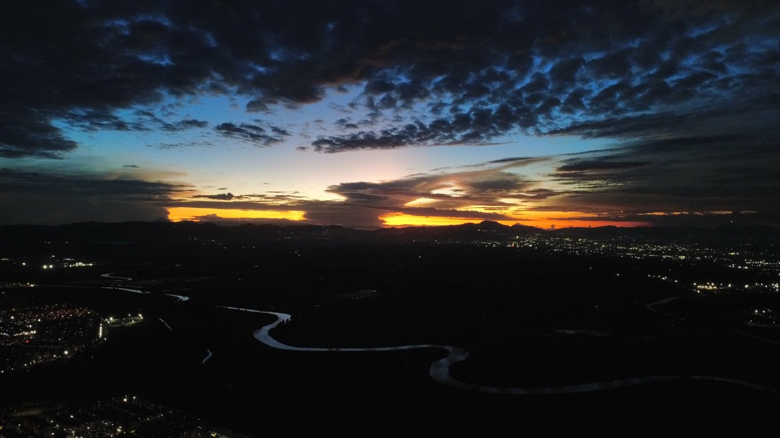 Atardecer aéreo sobre un valle colombiano con el río y las luces de un casco urbano